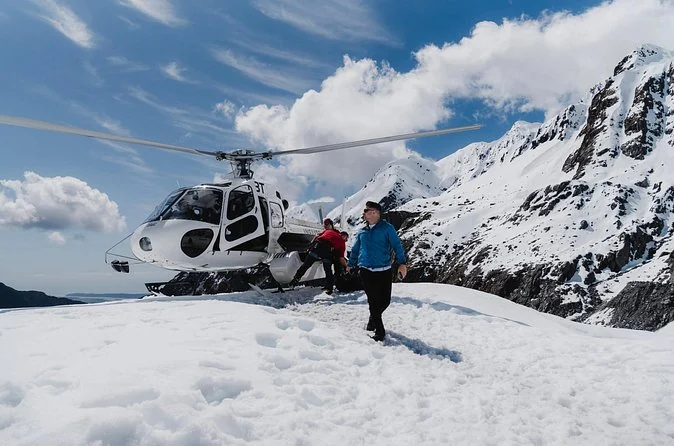 Ein Hubschrauber im Schnee, aus dem Passagiere und ein Guide aussteigen