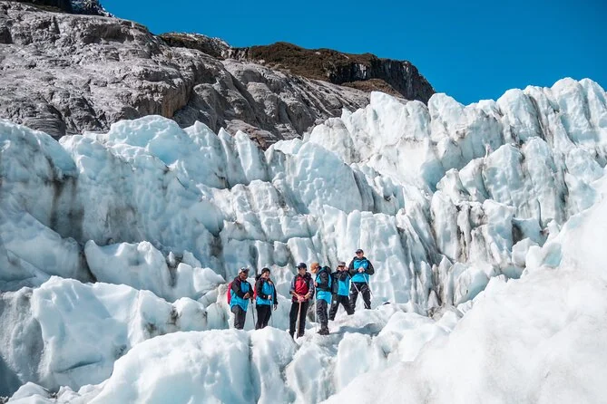 Wanderer in blauen Jacken, die zwischen weißen Eisrücken unter blauem Himmel gehen