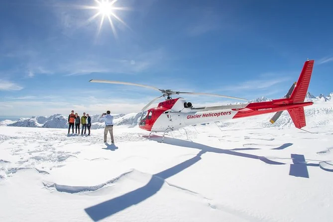 Passagiere im Schnee neben einem roten Hubschrauber hoch in den Bergen