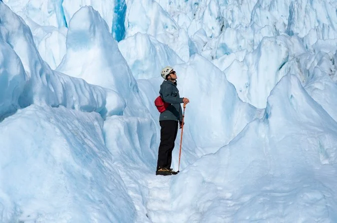 A hiker in a helmet standing beside a towering wall of white glacier ice