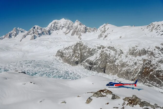 Ein Hubschrauber, gelandet auf einem Schneefeld über einem von Gipfeln umringten Gletscher