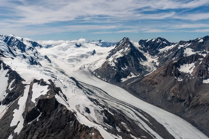 Ein langer Gletscher, der sich zwischen dunklen Bergen windet, aus der Luft gesehen